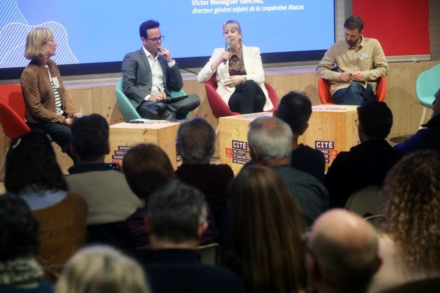 Plan large de la conférence avec le public et les intervenants du deuxième plateau.